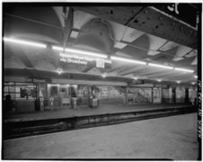 U-Bahnhof 96th Street um 1970 in einem Übergangsstadium mit Glühlampen und Leuchtstofflampen, mit noch weißem Unimark-Linienemblem auf schwarzem Stationsschild, mit noch nicht abgesperrtem oder vermauertem Seitenbahnsteig