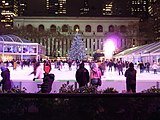 Eine Eisfläche im Park, mit geschmückten Weihnachtsbaum und Eisläufern.