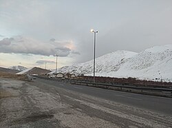 A photo taken in Tureh Iran, 2023. A road can be seen next to snow covered hills.