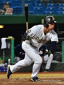 A man on a Baseball field in an Orix Buffaloes Uniform wearing a batting helmet starting a run from the batter's box.