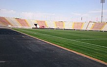 A photo taken close to the touchline showing part of the grass field and the stadium seating surrounding it