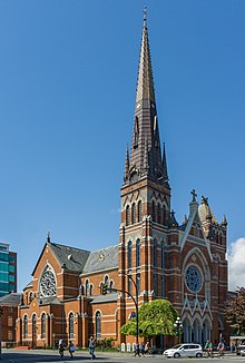 Exterior view of a red brick cathedral with a large spire built into a corner