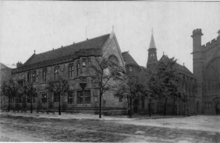 "Black and white photo of two storey mid-sized neo-gothic buildings next to the cathedral"