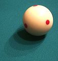 A "measel ball", the relatively new, spotted cue ball used in televised tournaments in pool, and now also in snooker and carom billiards as well. The spots help demonstrate the ball-spin effects of "english". Many actual players, not just audience members, favor these balls for the same reason, and they are especially good for practice, to ensure that one has a straight stroke. (Cropped closeup.)