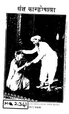 Cover-page of a script titled Saint Kanhopatra (संत कान्होपात्रा) in Marathi, with a photograph showing a woman dressed in a sari kneeling with palms pressed together before a man. The man, dressed in a white dhoti-kurta, is bent forward and seems to be blessing her with his wight hand placed over her head.