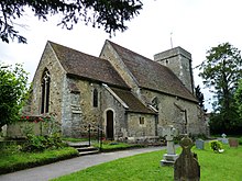 A photograph of a small church with a steep V-shaped roof and a square tower at the far end