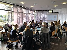 14 Personen sitzen um einen Tisch und sehen eine Powerpoint-Folie über WikiData