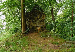 Mauerstück der ehemaligen Burg mit Hinweisschild, rechts der Steilabhang