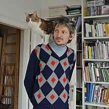 Andrea Lissoni 2016 mit Katze auf der Schulter vor einem Bücherregal