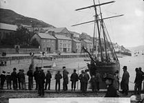 Men standing on a quay with a sailing ship in the background