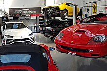 Inside the Eurospares workshop, showing a collection of luxury sports cars, including a Ferrari and a Lamborghini, with several showing signs of damage and in need of dismantling.