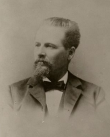 A black-and-white portrait photo of a mustached Kimball wearing a suit and bow tie