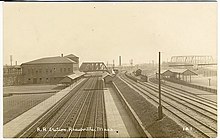 A black-and-white postcard of a two-story station at a complex railway junction