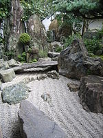 Rock garden with raked gravel and large stones including one placed like a bridge.