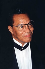 1997 photo of Farrakhan, the leader of the NoI. He is staring to the right, away from the camera, and wearing a suit.