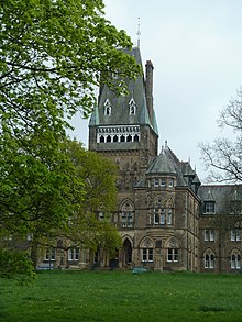 Victorian stone building with ornate central tower, set in lawns and partly hidden by trees