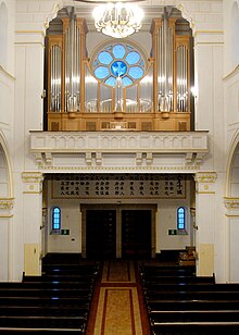 Interior of the end of the cathedral showing the main door with a choir loft above it on which stands a large pipe organ above which is a blue rose window with a dove at its centre