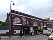 A red-bricked building with a rectangular, white sign reading "KENTISH TOWN STATION" in black letters all under a light blue sky