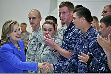 Clinton greeting U.S. military personnel at Andersen Air Force Base in Guam. The personnel are wearing uniforms and standing side by side.
