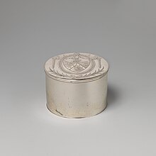 small cyclindrical box engraved with a coat of arms on the top