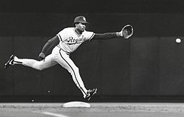 A man in a light baseball jersey and dark cap