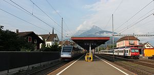 Island platform with passing trains and a station building to the right