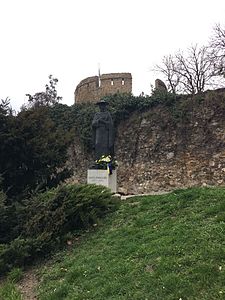 Janus Pannonius szobra, a háttérben a barbakán látható