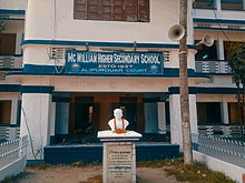 Statue of Nilkanta Mukherjee in front of school building. The sign board of McWilliam HS School visible in the background.