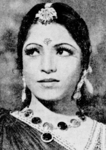 A young Indian woman wearing jewelry on her head, ears, and neck, and a dark sari