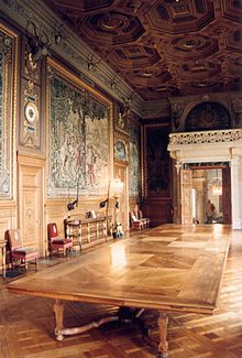 Grande table de réception au centre avec des tapisseries aux murs et un plafond à caissons