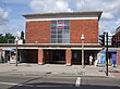 A red-bricked building with a rectangular, grey sign reading "SUDBURY HILL STATION" in black letters all und er a blue sky with white clouds