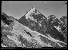 Schwarz-weiß Fotografie eines spitzen Berggipfels mit Schnee und Eismassen auf dunklem Fels
