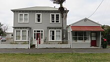 A blue-gray two-storey building next to a smaller storefront