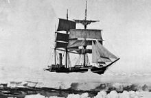 Three masted ship with sails spread, surrounded by pack ice, with a narrow lane of water in the foreground