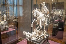 A table-top sized statue in ivory of a mounted figure. The horse is reared-backward, trampling a supine figure representing the "horrors of war."