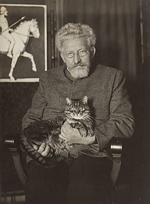 Der bereits grauhaarige Michael Georg Conrad mit Katze auf dem Schoß in seiner Wohnung. Aufnahme undatiert.