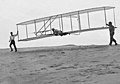 Sayısız testlerden birinde, 1902 Wright Planörü'nün üstünde Wilbur Wright, solda Orville Wright, sağda arkadaşları Dan Tate, (10 Ekim 1902).