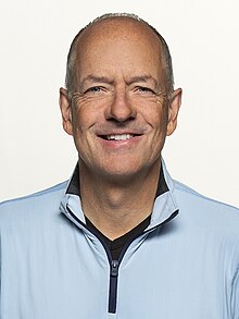 Andrew Witty, a bald, clean-shaven white man, wearing a light blue suit.