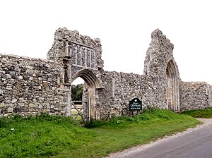 A stone wall with two large arches, one of which contains a wooden gate, with a sign in front of them reading "Welcome to Greyfriars medieval friary"