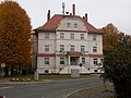 Wohnhaus in offener Bebauung (ehemaliges Gemeindeamt), mit Einfriedung, Vorgarten, Pflaster, zwei Pfeiler einer Toreinfahrt, Feuerwehrhaus mit Anbau und Waschhaus sowie Lindenhain