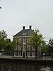 Amstelrank (of voormalige Nederlandse Hervormde Diaconie Bestedelingenhuis). Vrijstaand vierkant huis onder schilddak waarop vier schoorstenen. Dakkapel, deuromlijsting, stichtingssteen. Oorspronkelijke roedenverdeling. Tuinmuren t.w.z. van de gevel, in de linkse gebosseerde hekpijlers