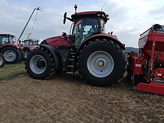 Zijaanzicht van een rode tractor met achterop een woeler en daarachter een zaaimachine