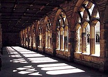 Seitliche Farbfotografie von einem Kreuzgang mit Blick in den Innenhof. Durch die mittelalterlichen Rundbögen fällt das Tageslicht auf den Boden. Die dunkle Decke ist kaum zu erkennen.