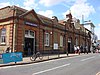 A red-and-brown bricked building with a rectangular, dark blue sign reading "UPTON PARK STATION" in white letters all under a light blue sky