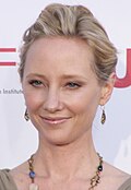 A woman with blond hair, wearing a beige earrings and necklace.