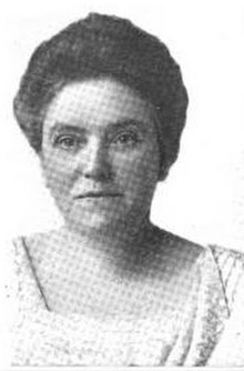 A white woman with her hair in a bouffant updo, wearing a square-necked bodice.