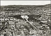 Flyfoto av Oslo sentrum, trolig fra 1950-tallet, med blant annet Karl Johans gate som ender i Slottsbakken med Slottsplassen foran Slottet. Postkort: Nasjonalbiblioteket