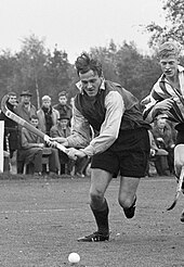 Schwarzweißfoto vom spielenden Zweerts in dunkler Hose und dunklem Trikot mit weißen Ärmeln. Er hält den Schläger in beiden Händen und schaut auf den Ball vor ihm.