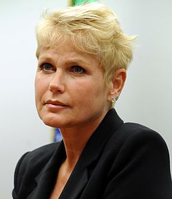 A blonde woman speaking into a microphone against a blue background