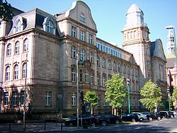 Das Görres-Gymnasium ist mit seiner viergeschossigen neubarocken Hauptfassade nach Norden zur Bastionstraße ausgerichtet. Links an der Ecke das Gebäude des Gymnasiums zur Königsallee hin. An der Ecke vor dem Gymnasium der Neckerei-Brunnen